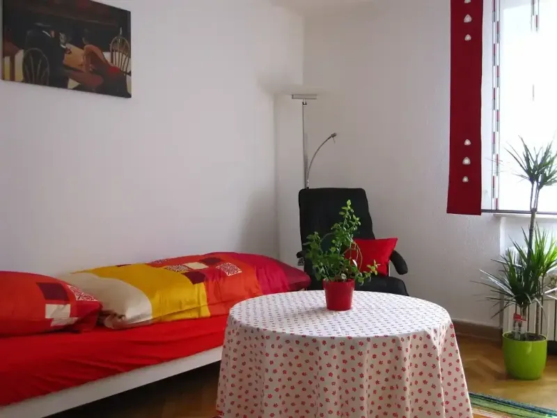 eeinzelschlafzimmer mit bett tisch stehlampe und relaxsessel sowie grosser zimmerpflanze