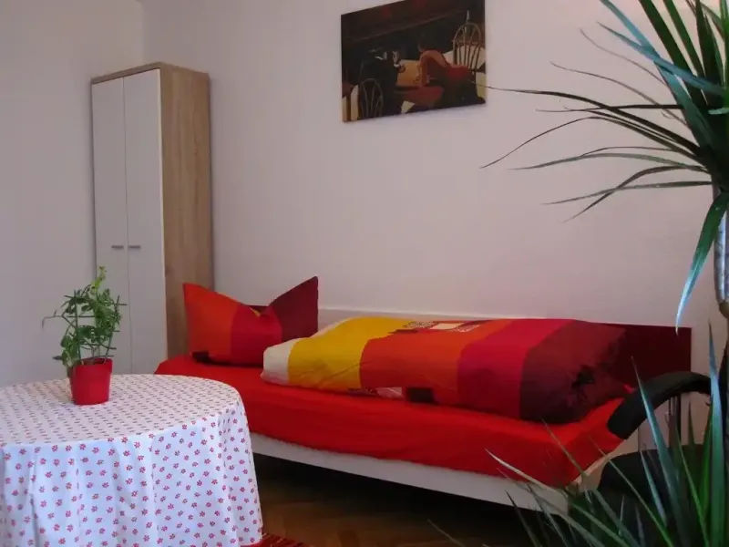 einzelschlafzimmer mit bett kleiderschrank tisch und wandbild sowie grosser zimmerpflanze